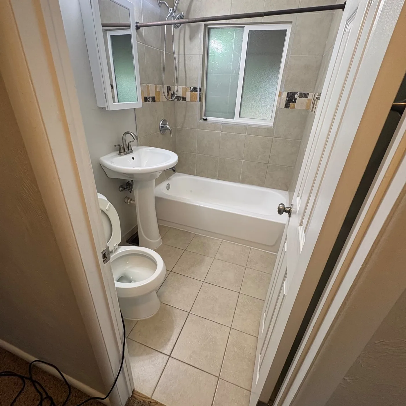 Empty apartment bathroom with clean tile floor, white tub and toilet ready for the next tenant
