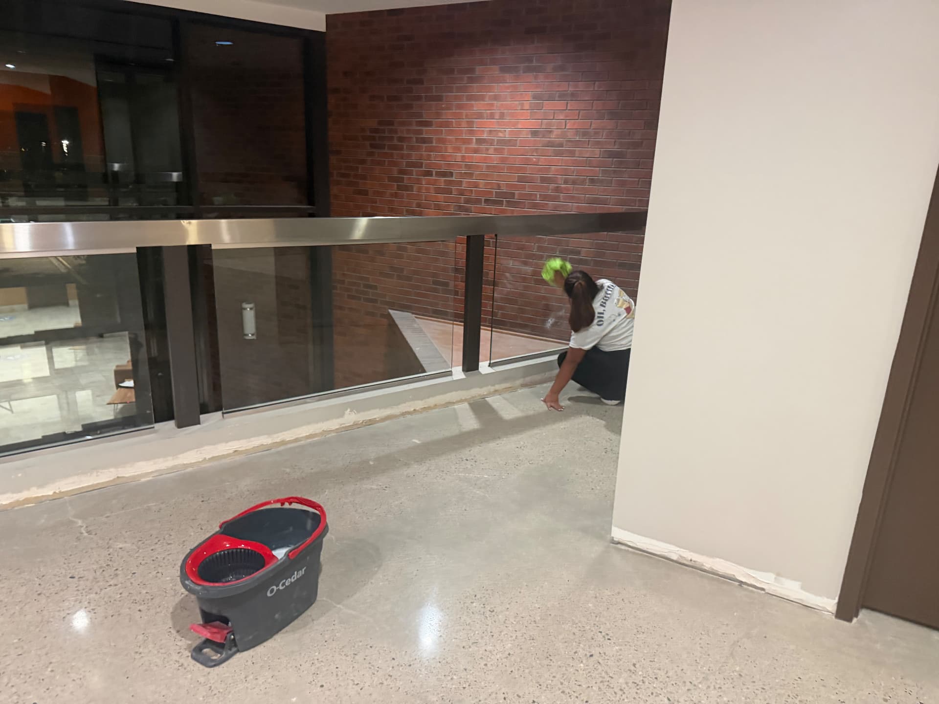 Hello Clean & Company crew member hand-detailing glass railing and floor edges during a commercial construction cleanup