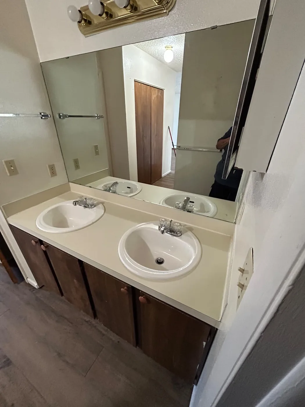 Older double vanity with wood cabinets and a large mirror cleaned in a rental bathroom