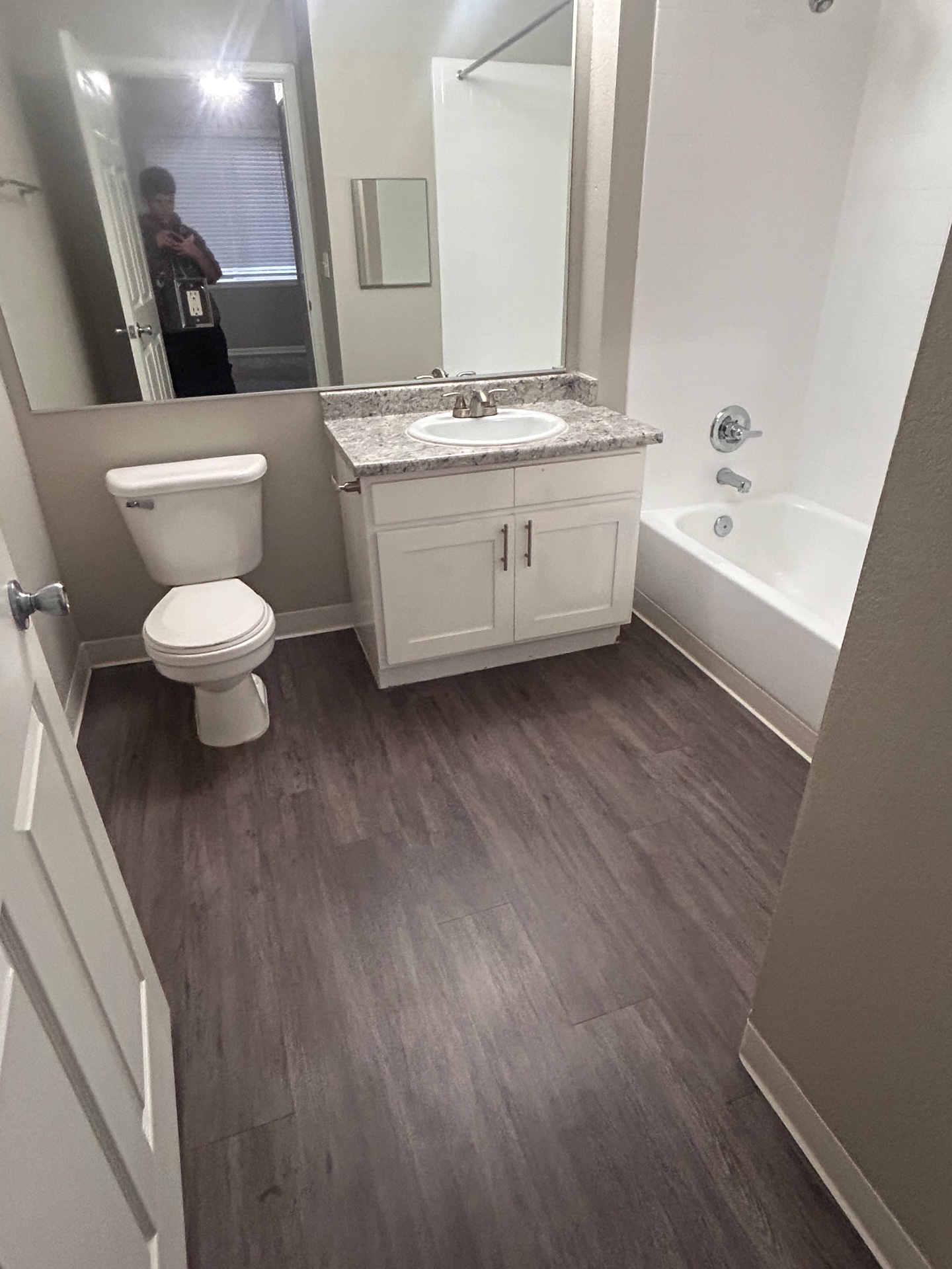 Vacant bathroom with clean vinyl plank floor, vanity, toilet and tub after a move-out cleaning