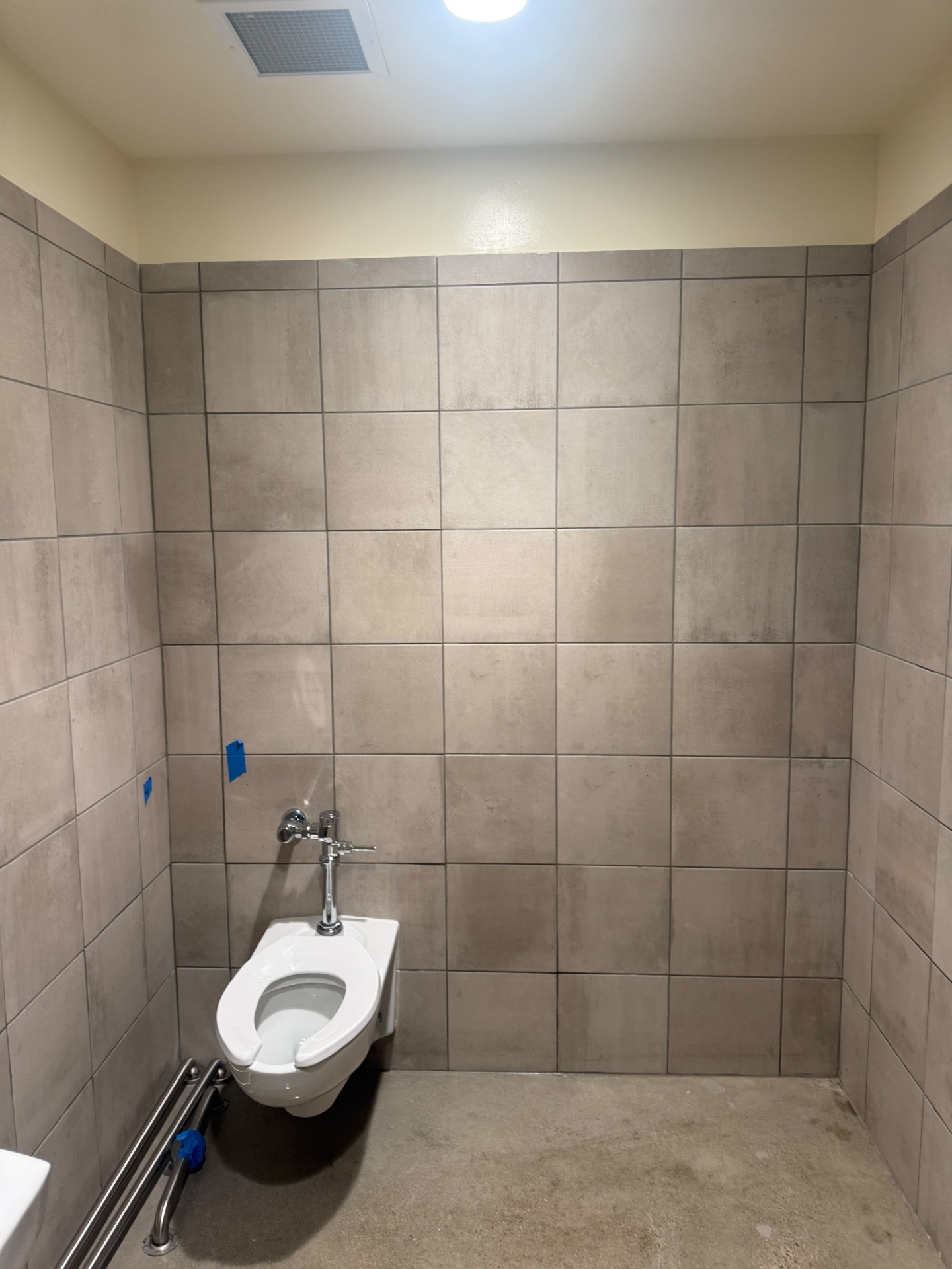 Commercial restroom with tile walls and wall-mounted toilet during a post-construction final clean